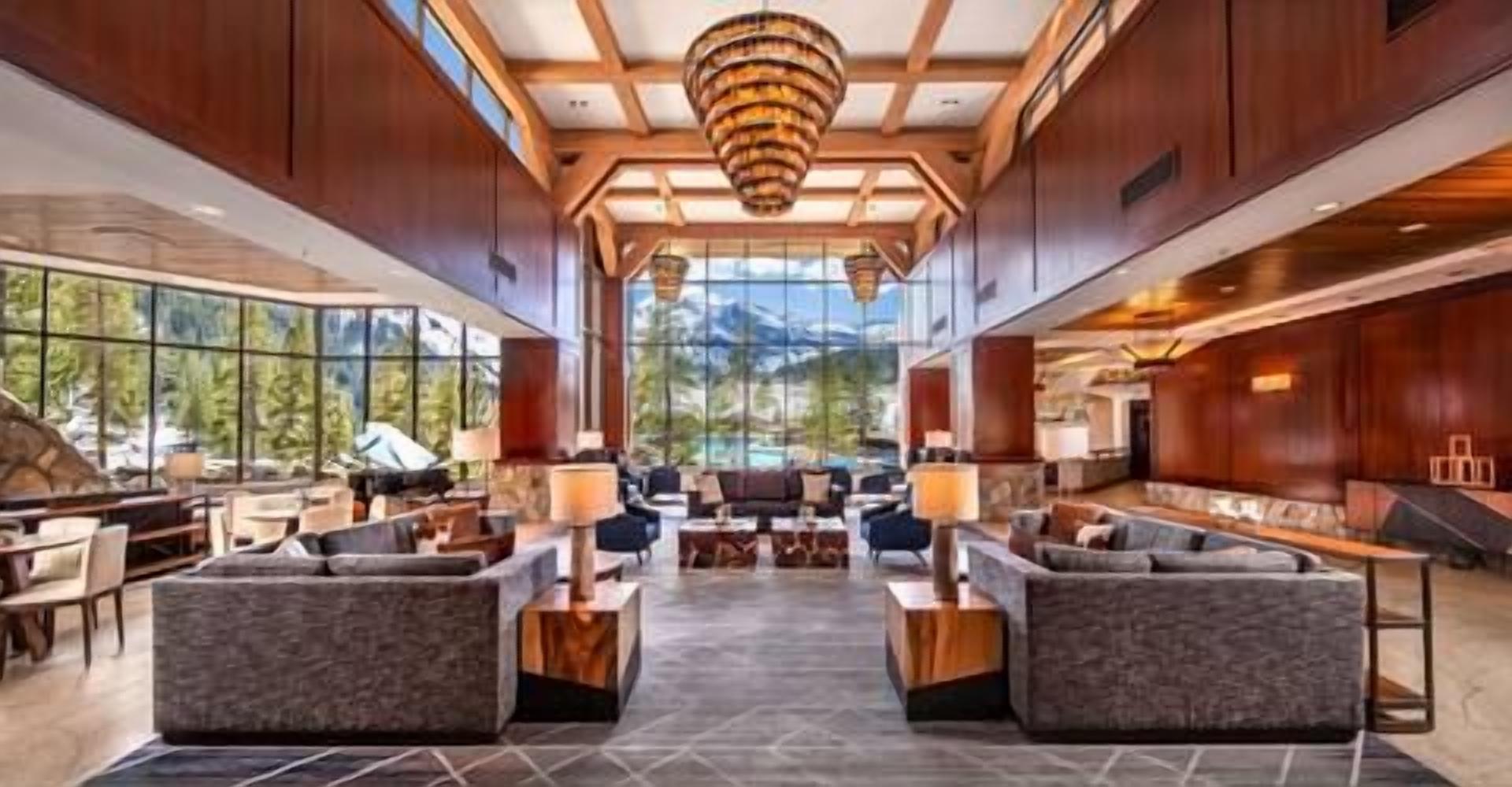 Un hall d’entrée spacieux avec un espace salon central, de grandes fenêtres offrant une vue sur les montagnes et un lustre moderne.