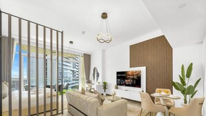 En moderne stue med sofa, spisebord, stole, et fjernsyn og et stort vindue med udsigt over byen.