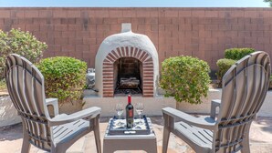 An outdoor seating area with two chairs and a table, a brick oven, and a bottle of wine. - Covered Patio, Lava Rock Gas Fire Pit, Near Spring Training, Golf, Hiking & Biking; 30 Day Min (Gilbert)