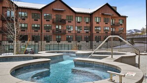 A modern building with a pool area, including a hot tub and a small pool, surrounded by a fence.