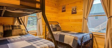 A cabin with two bunk beds, a wooden interior, and a window with curtains.