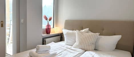 Habitación de hotel con cama, ventana con vistas, un jarrón con flores y una lámpara.