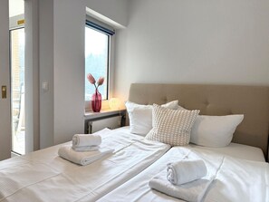 Een hotelkamer met een bed, een raam met uitzicht, een vaas met bloemen en een lamp.
