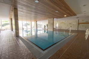 Une piscine intérieure dotée d’un plafond en bois, de grandes fenêtres et d’un sol carrelé.