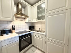 Una cocina con armarios blancos, una campana extractora de acero inoxidable, horno empotrado, estufa y un lavabo.