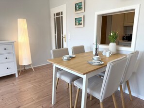 A dining area with a wooden table, four chairs, a lamp, and a view of the kitchen through a window.