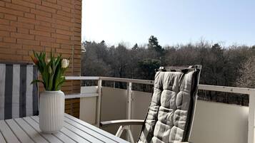 Ein Balkon mit einem weißen Tisch, einem Stuhl mit kariertem Sitzkissen und einer Vase mit Blumen.