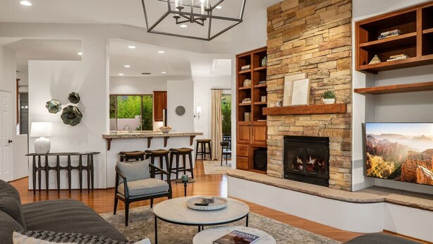 A modern living room with a stone fireplace, a dining area, and a kitchen in the background. - Luxe 4-BR Home: Spa, Red Rock Views, and A+ Trails (Sedona)