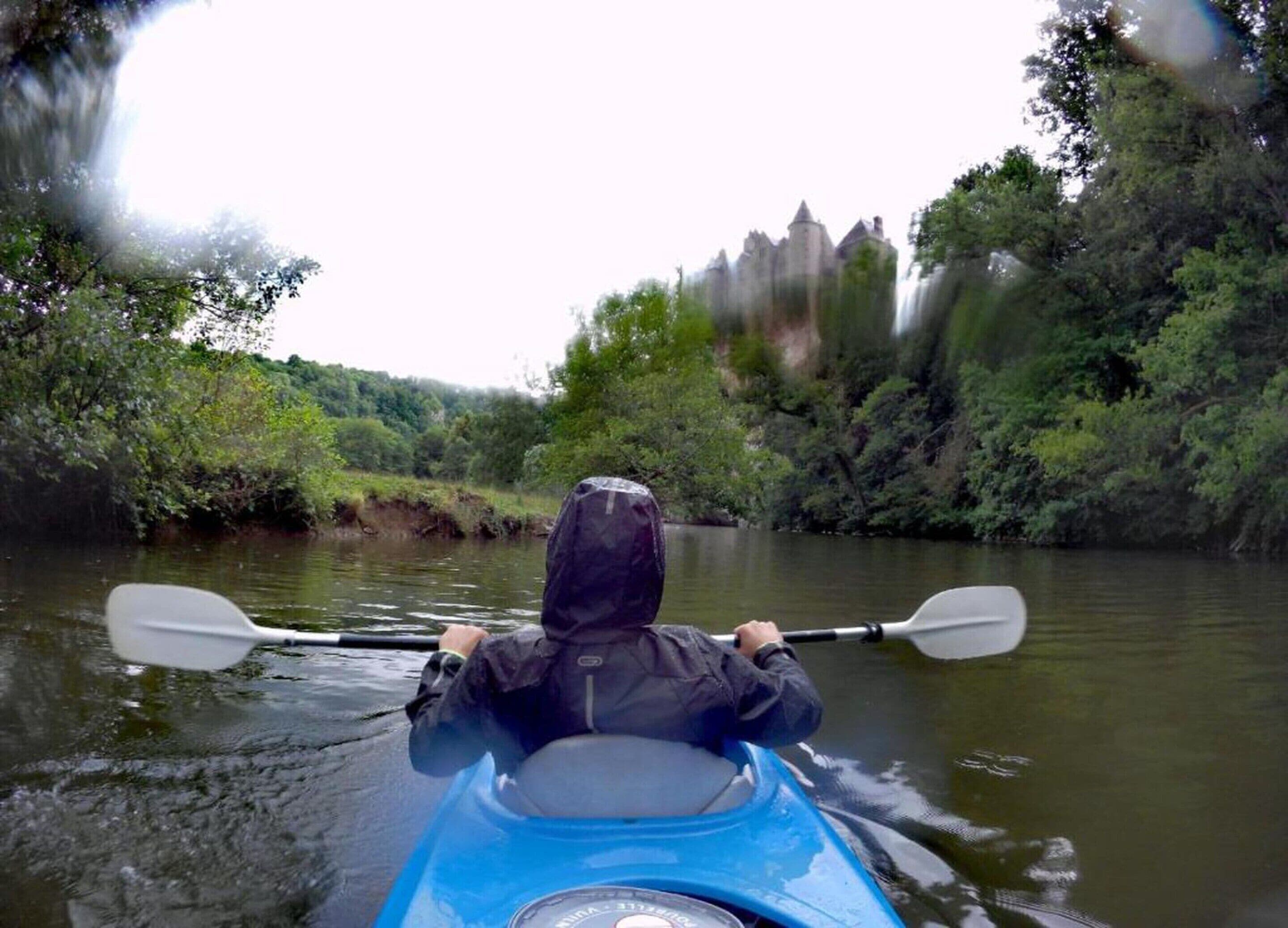 A person kayaking on a river with a castle in the background.