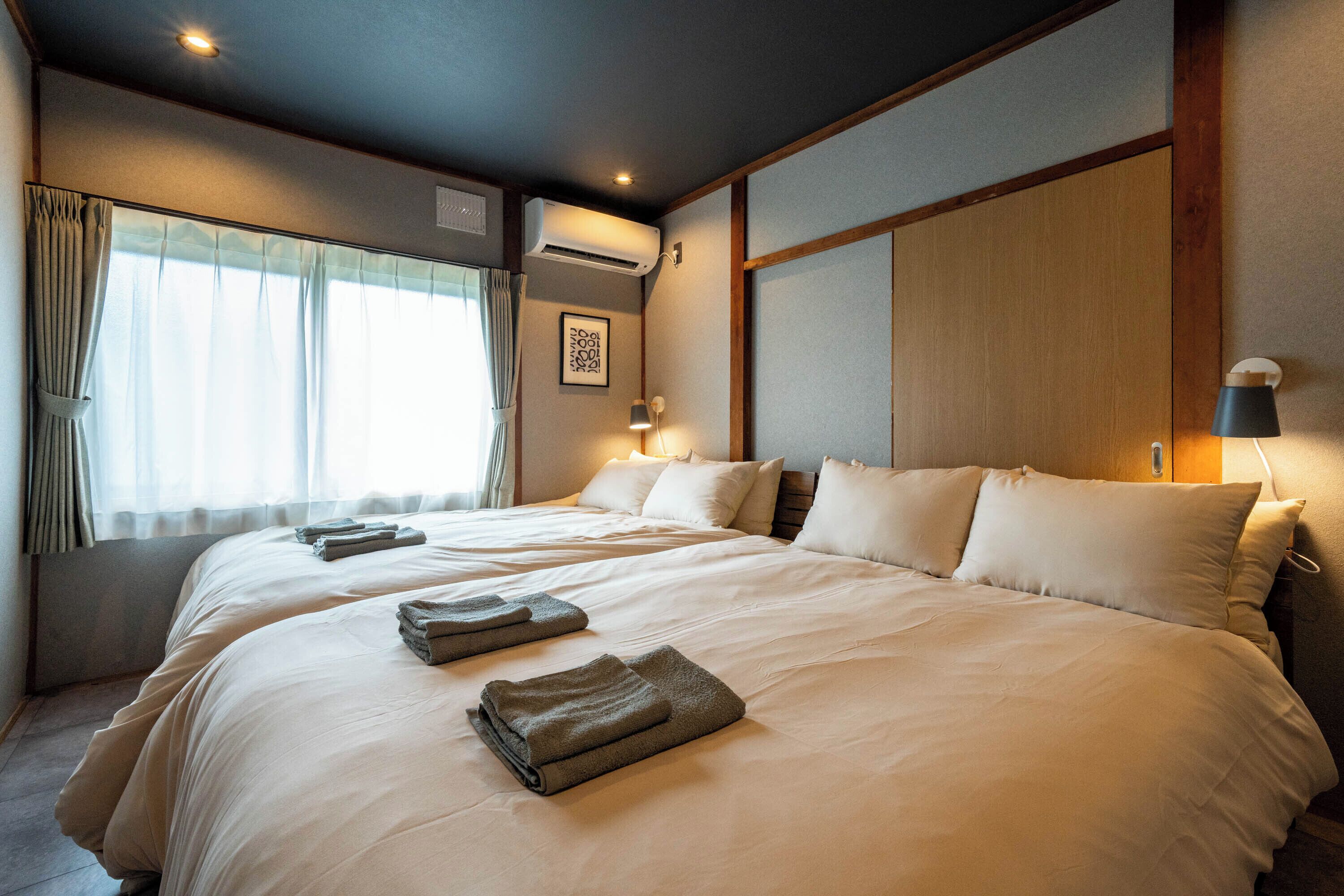 A hotel room with a large bed, two bedside tables, a window with curtains, and an air conditioning unit.