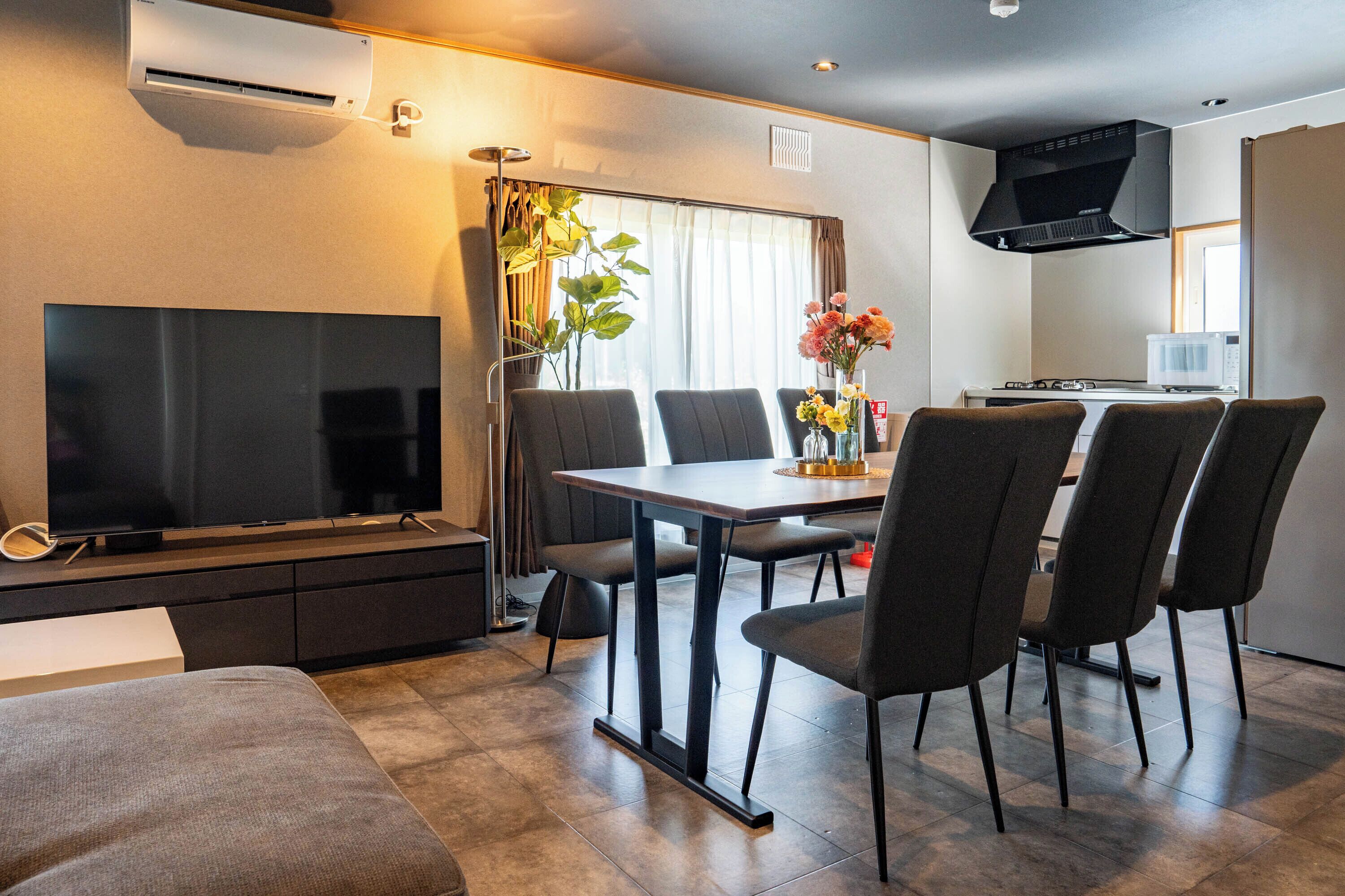 Una sala de estar moderna con un televisor de pantalla plana, una mesa de comedor con sillas, un sofá y una zona de cocina con microondas.