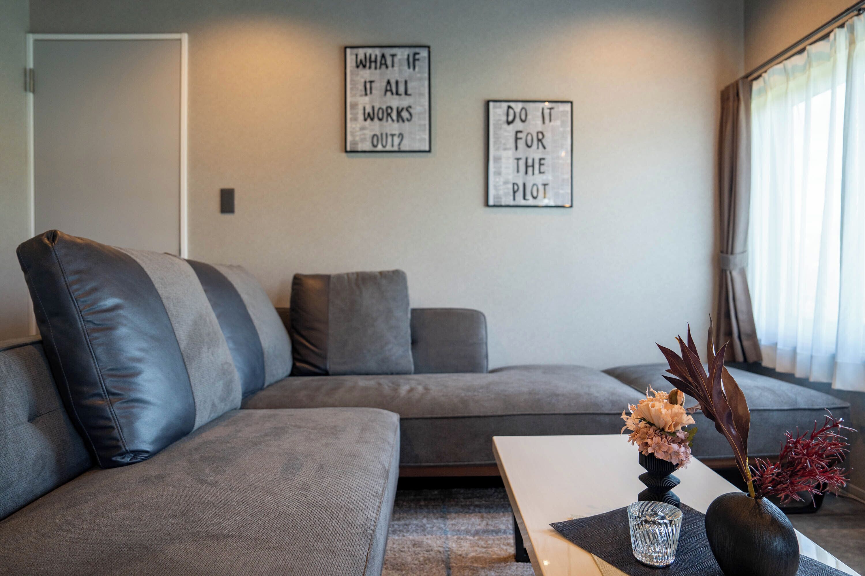 A modern living room with a grey sectional sofa, a small table, and two framed motivational quotes on the wall.