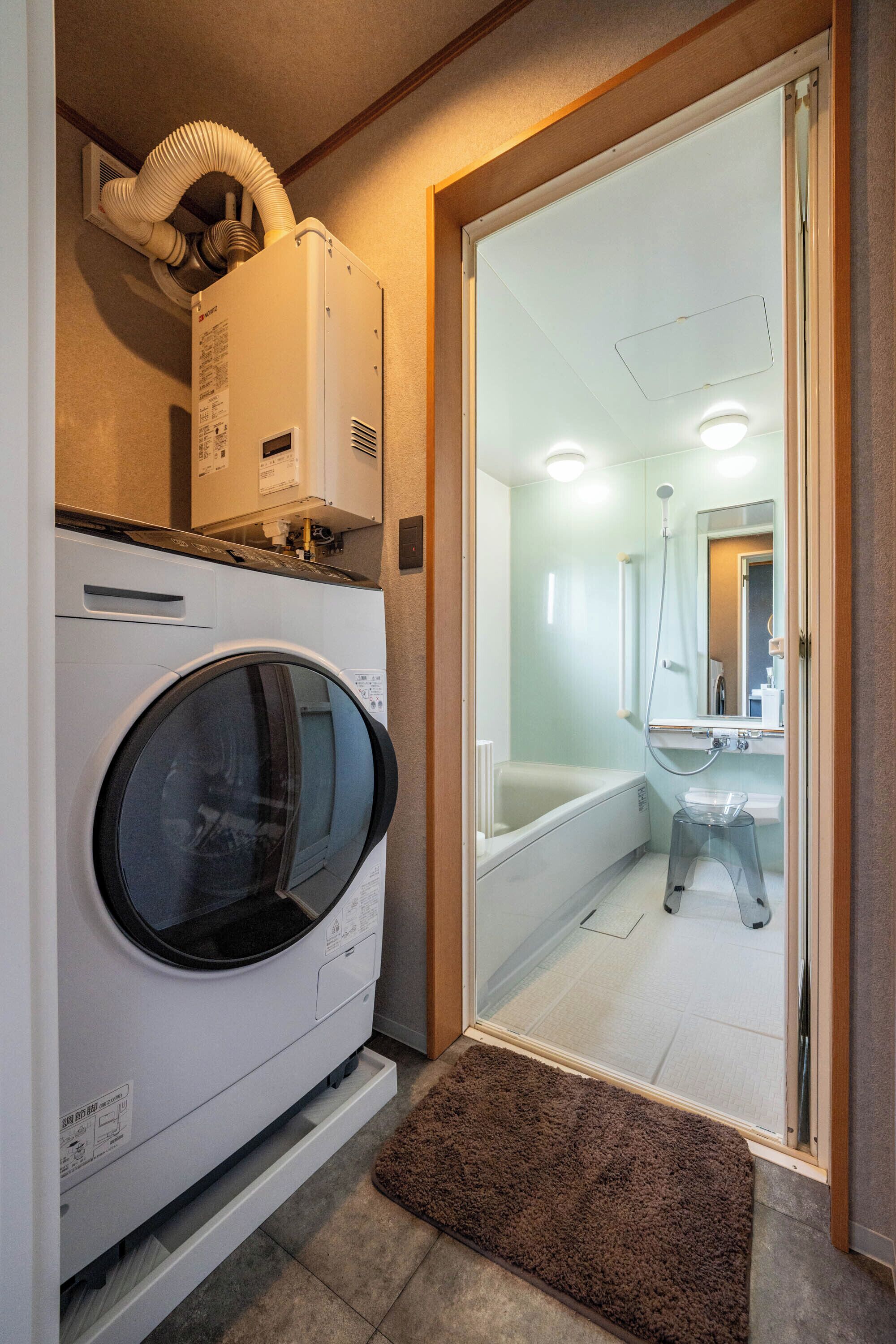A compact laundry room with a front-loading washer and dryer, a glass shower enclosure, and a small sink.