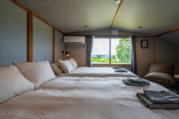 Ein Hotelzimmer mit zwei Betten, einem Fenster mit Vorhängen, einem Schreibtisch und einem Stuhl.