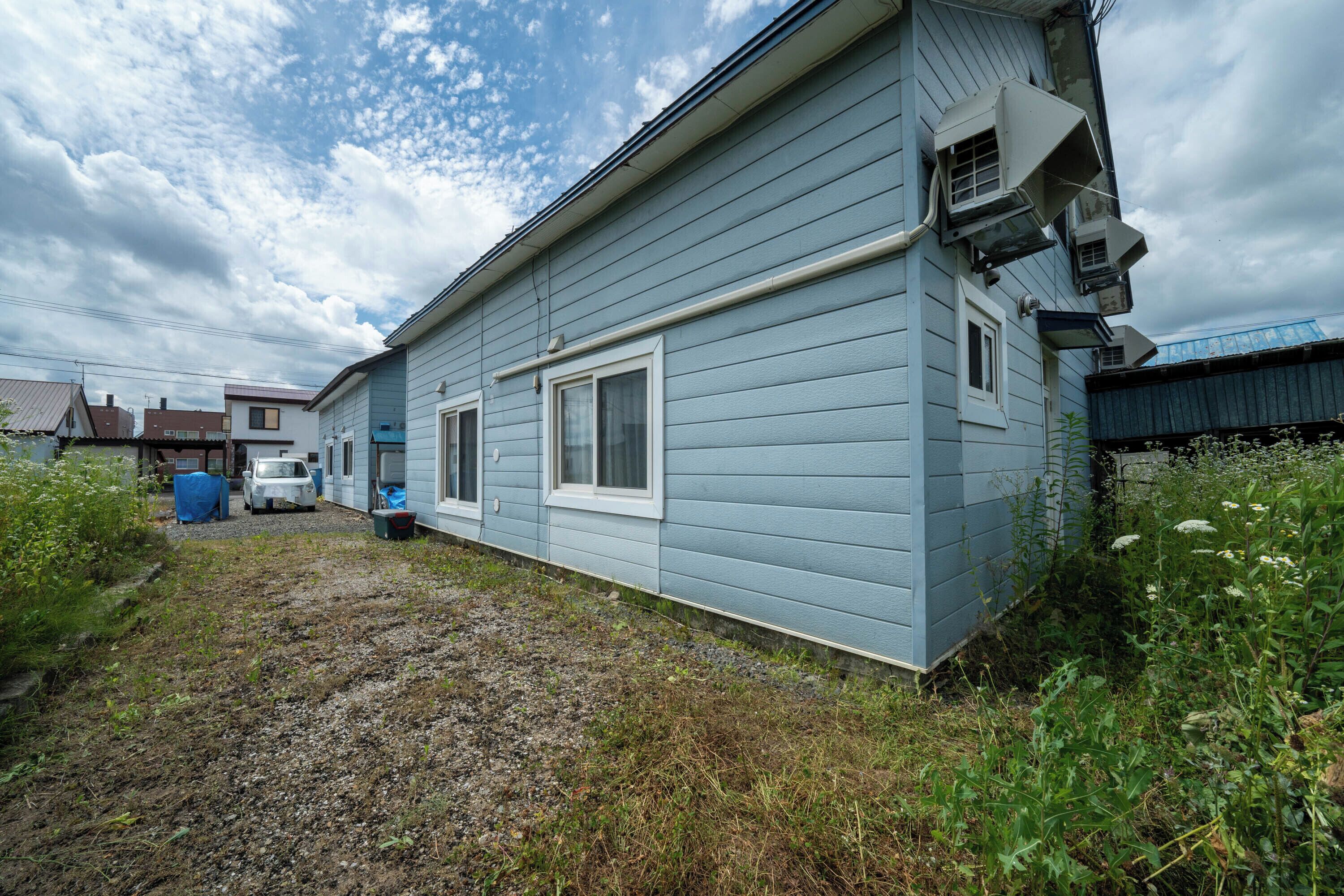 A single-story house with a blue exterior, a gravel driveway, and a small garden area.