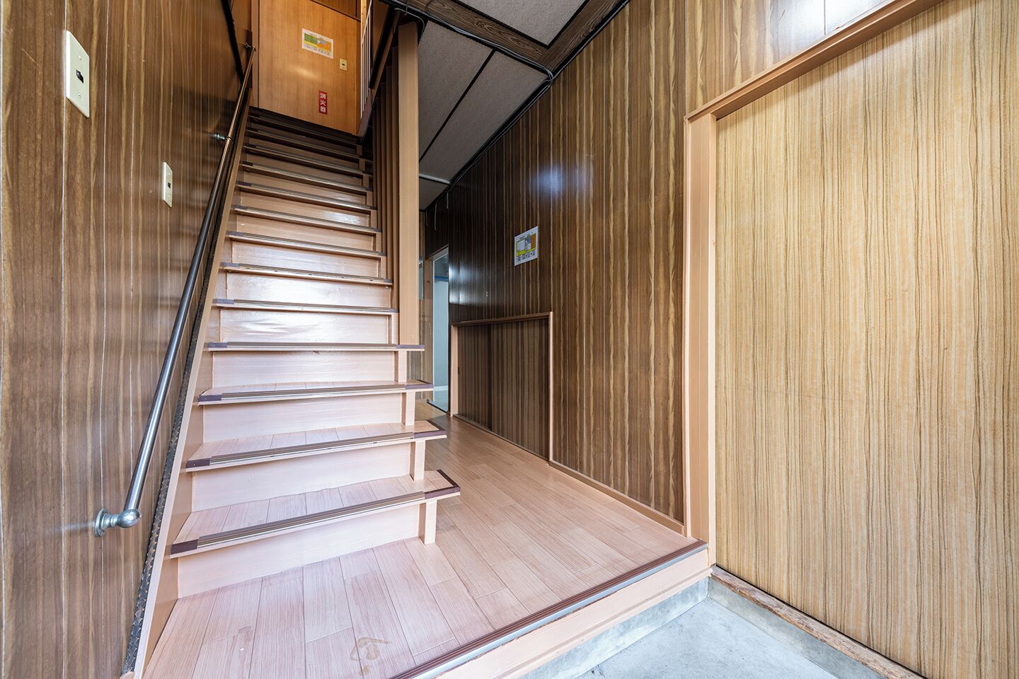 Una escalera de madera con barandilla de metal que lleva a una puerta con un cartel encima.
