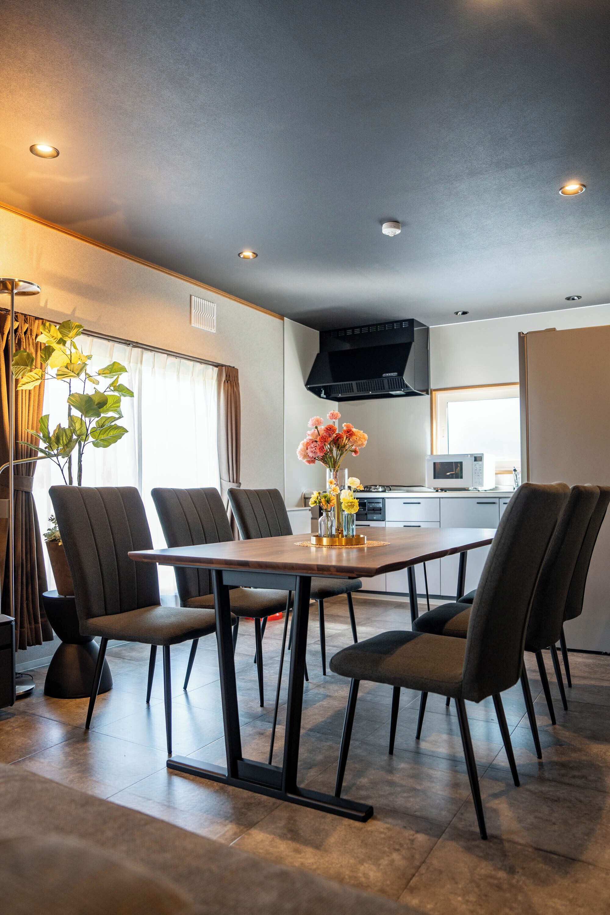 A modern dining area with a long table, six chairs, and a vase of flowers.