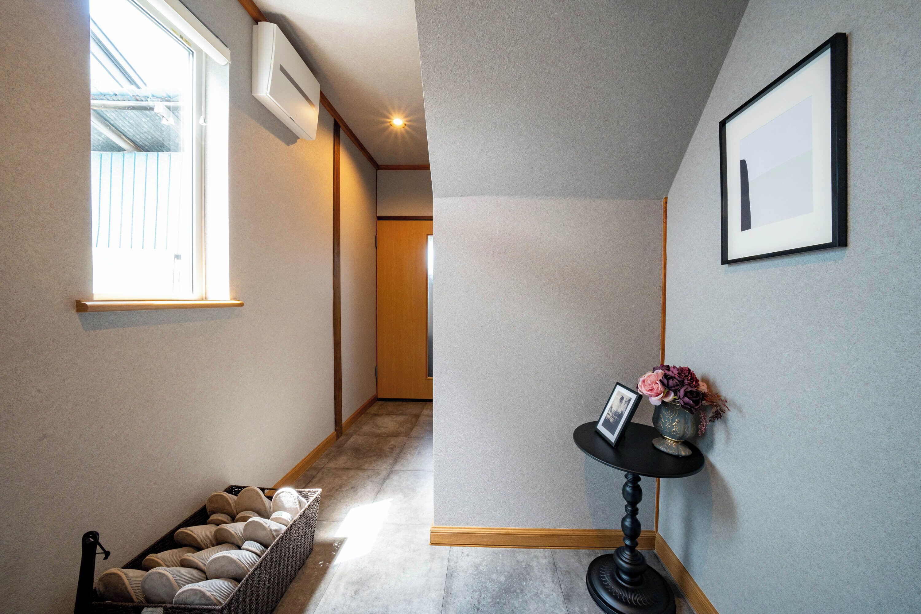 A hallway with a bench, a framed picture, and a vase with flowers.