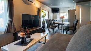 Ein modernes Wohnzimmer mit einem Flachbildfernseher, einem Couchtisch und einer Couch. Es gibt eine Essecke mit einem Tisch und Stühlen.