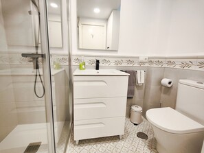 Un bagno moderno con doccia vetrata, un lavandino bianco con dispenser di sapone, un water e uno specchio sopra il lavandino.