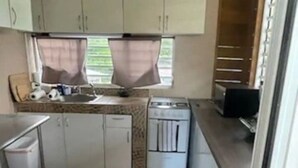 A compact kitchen with white cabinets, a sink, a stove, and a microwave.
