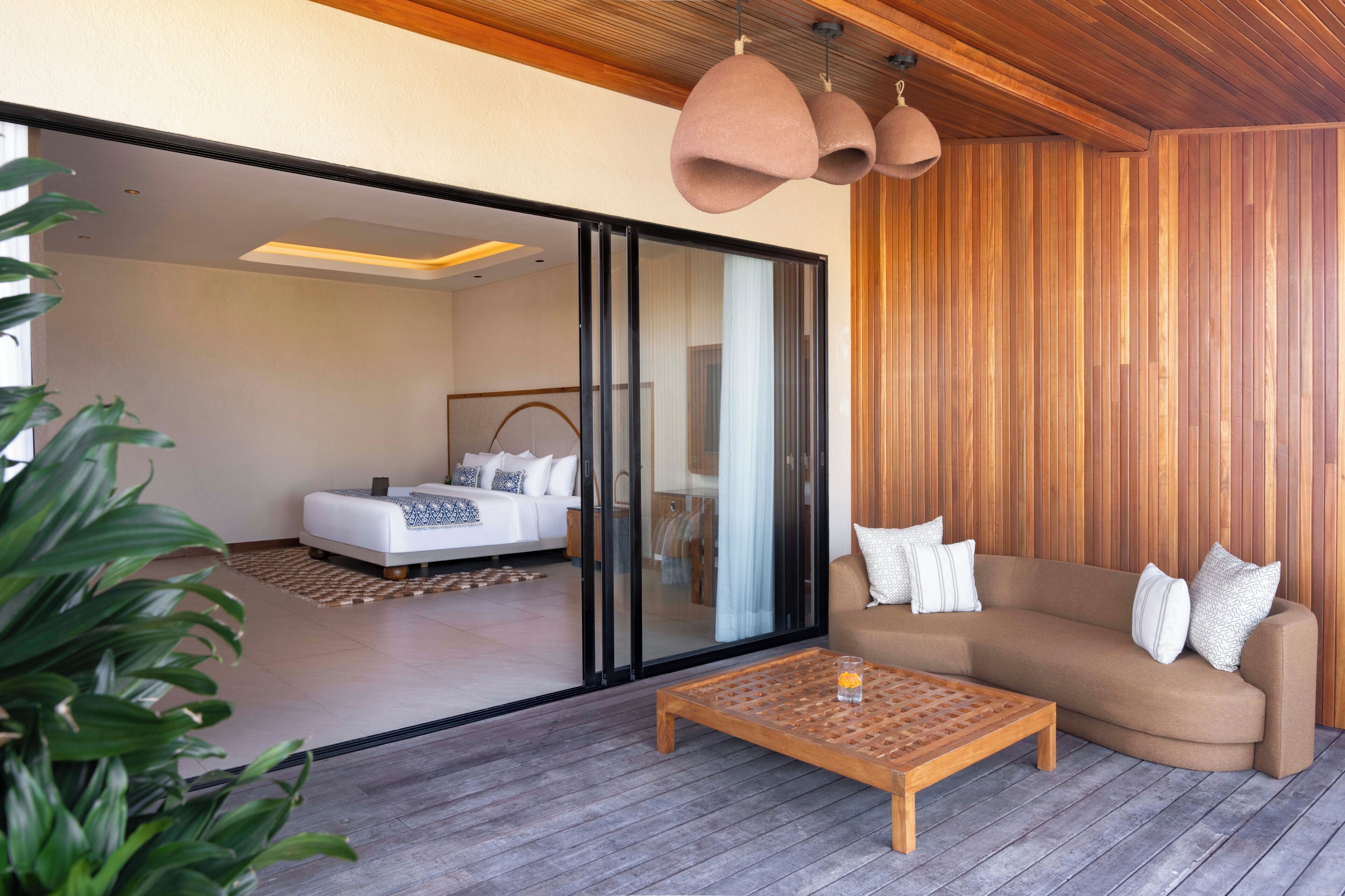 Una sala de estar moderna con un sofá, una mesa de centro y un ventanal corredera que da a un dormitorio.