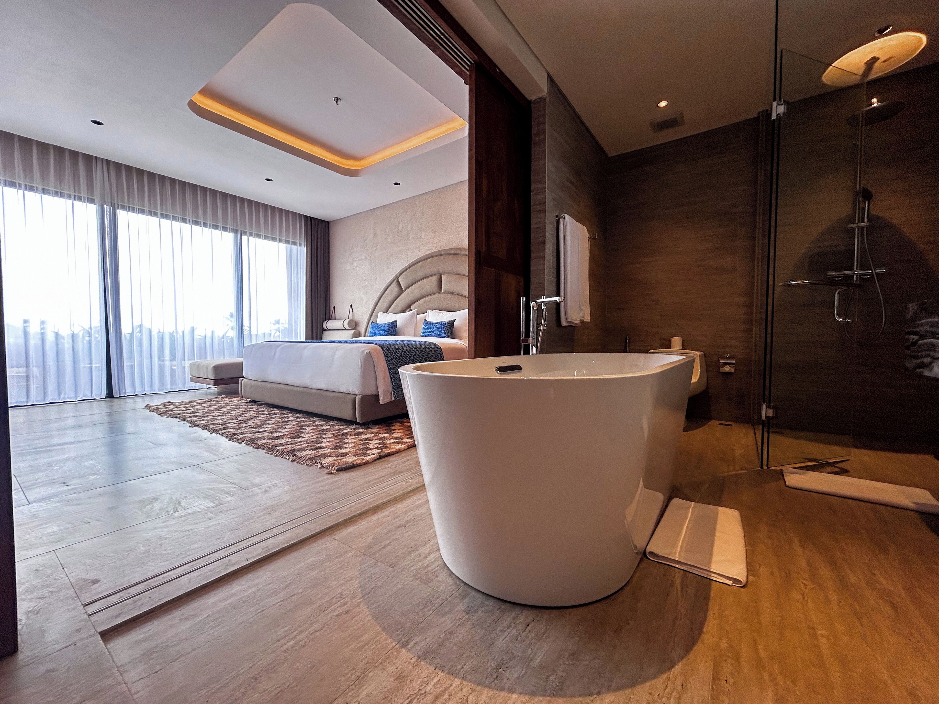 Ein modernes Hotelzimmer mit einem großen Bett, einer runden Badewanne und einer Dusche mit Glastrennwand.