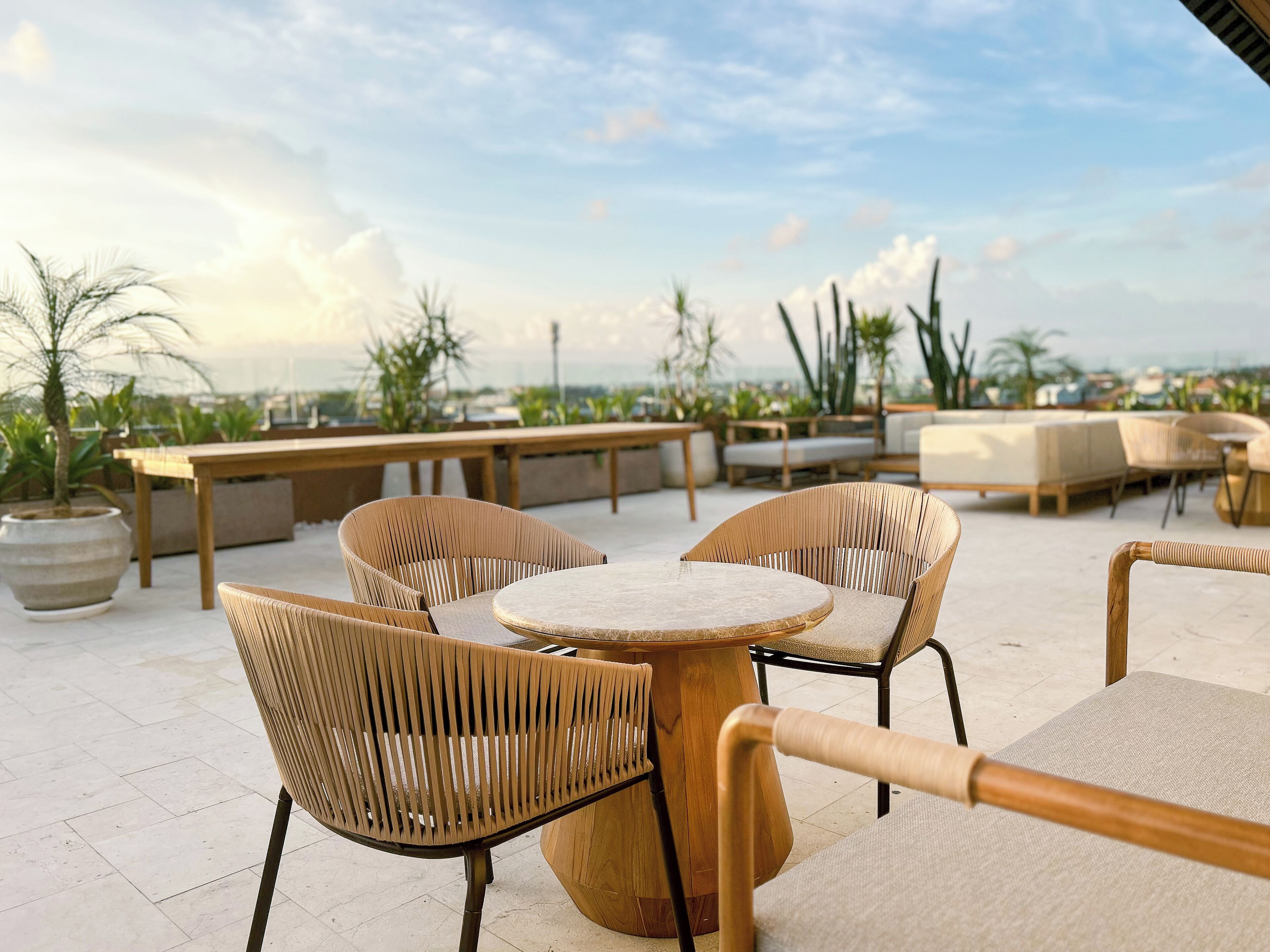 Una terrazza sul tetto con sedie e tavoli in vimini, piante in vaso e vista sulla città.
