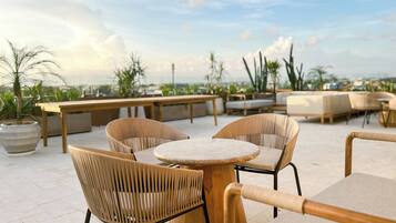 Una terraza en la azotea con sillas y mesas de mimbre, plantas en macetas y vistas a la ciudad.