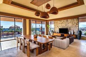 Un amplio salón con una mesa de comedor de madera, asientos cómodos, una pared de acento de piedra y un televisor grande.