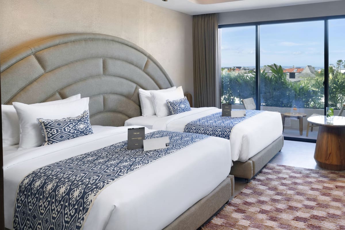 Une chambre d’hôtel moderne avec un grand lit, un lit plus petit et un coin salon offrant une vue sur la ville.