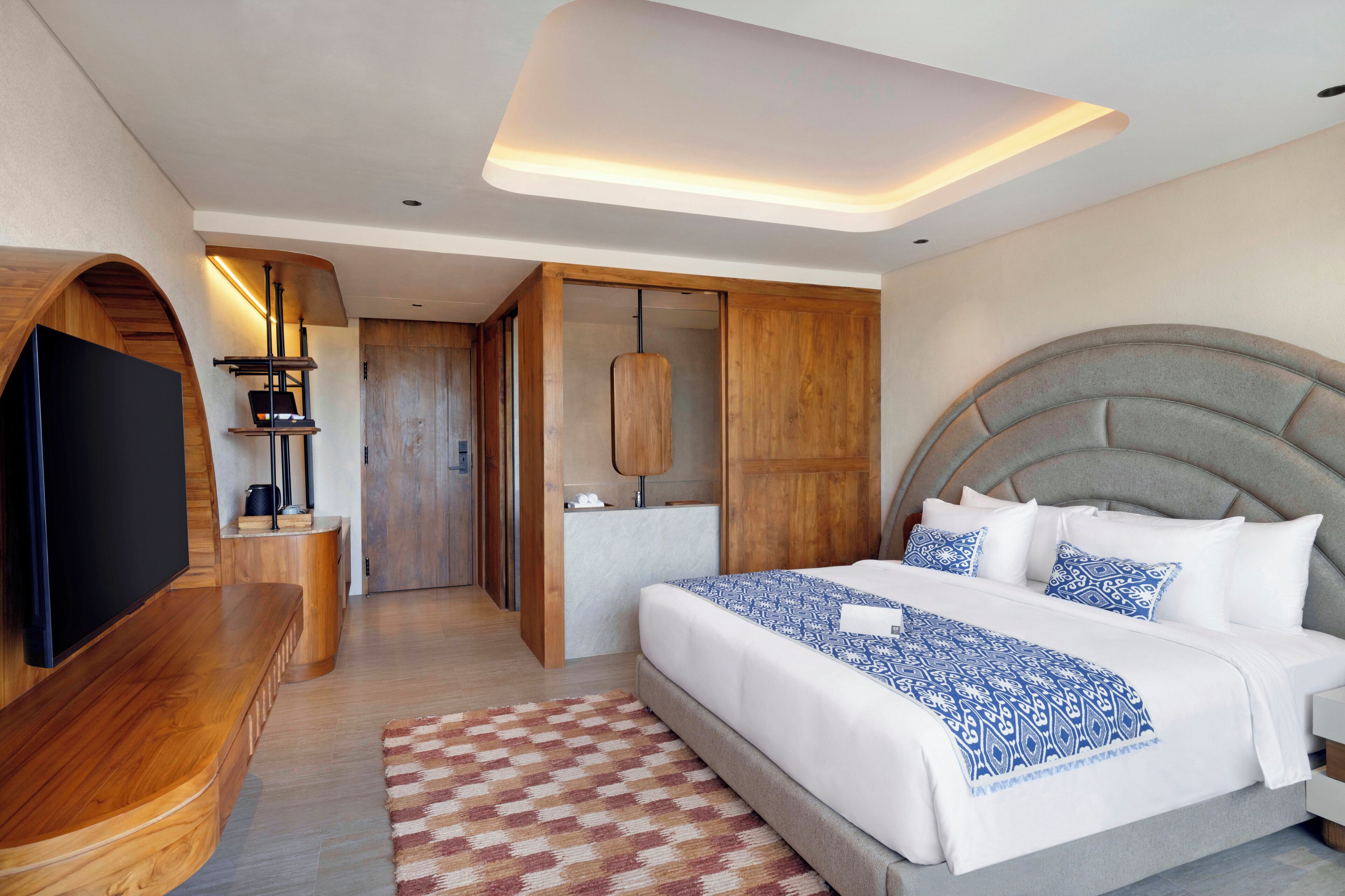 Una habitación de hotel moderna con una cama grande, un televisor de pantalla plana, un banco de madera y un armario empotrado.