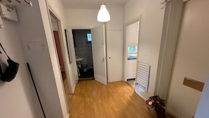 En gang med trægulv, hvide vægge og en hængende lampe.