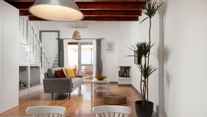 A modern living room with a grey sofa, white chairs, a dining table, and a large potted plant.