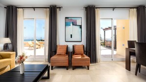 A hotel room with a sofa, two armchairs, a coffee table, a painting, and a view of the outside.