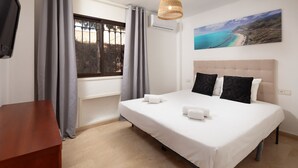 A bedroom with a bed, two pillows, a bedside table, a window with curtains, and a painting on the wall.
