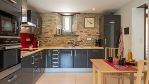 A modern kitchen with a stone wall, stainless steel appliances, and a dining area with a wooden table and chairs. - La Manoir du Moros by Interhome (Concarneau)