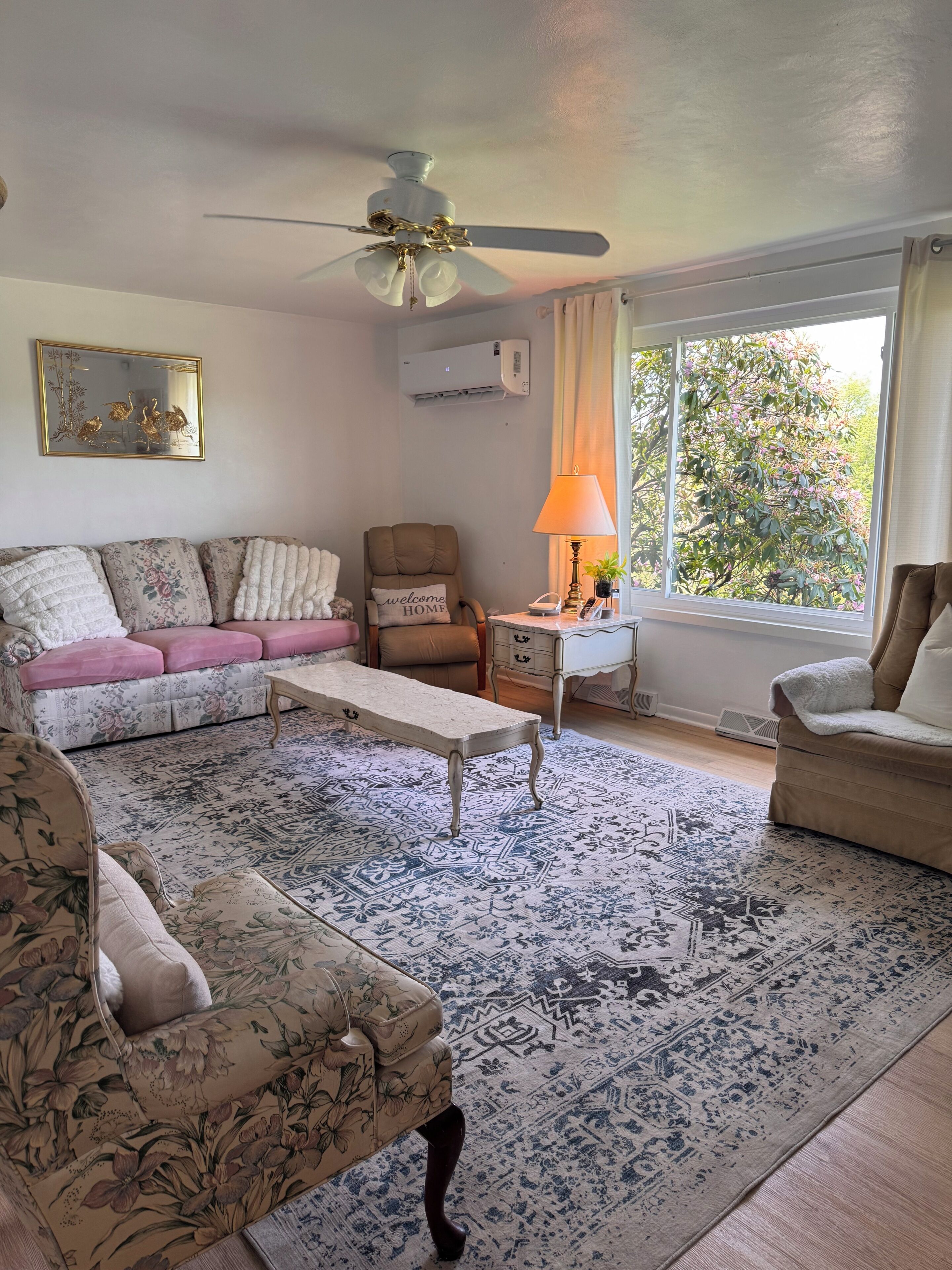 A living room with a ceiling fan, a sofa, a chair, a coffee table, and a window with curtains.