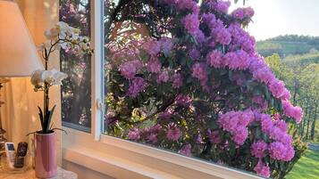 Une fenêtre donnant sur des fleurs violettes et une lampe blanche posée sur une table de chevet.