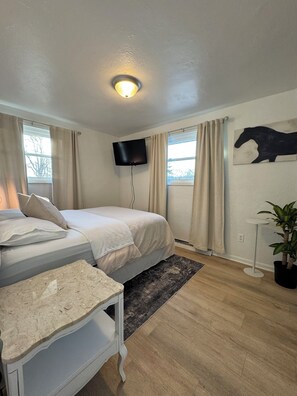 A bedroom with a bed, a bedside table, a TV mounted on the wall, a window with curtains, and a wall-mounted artwork.