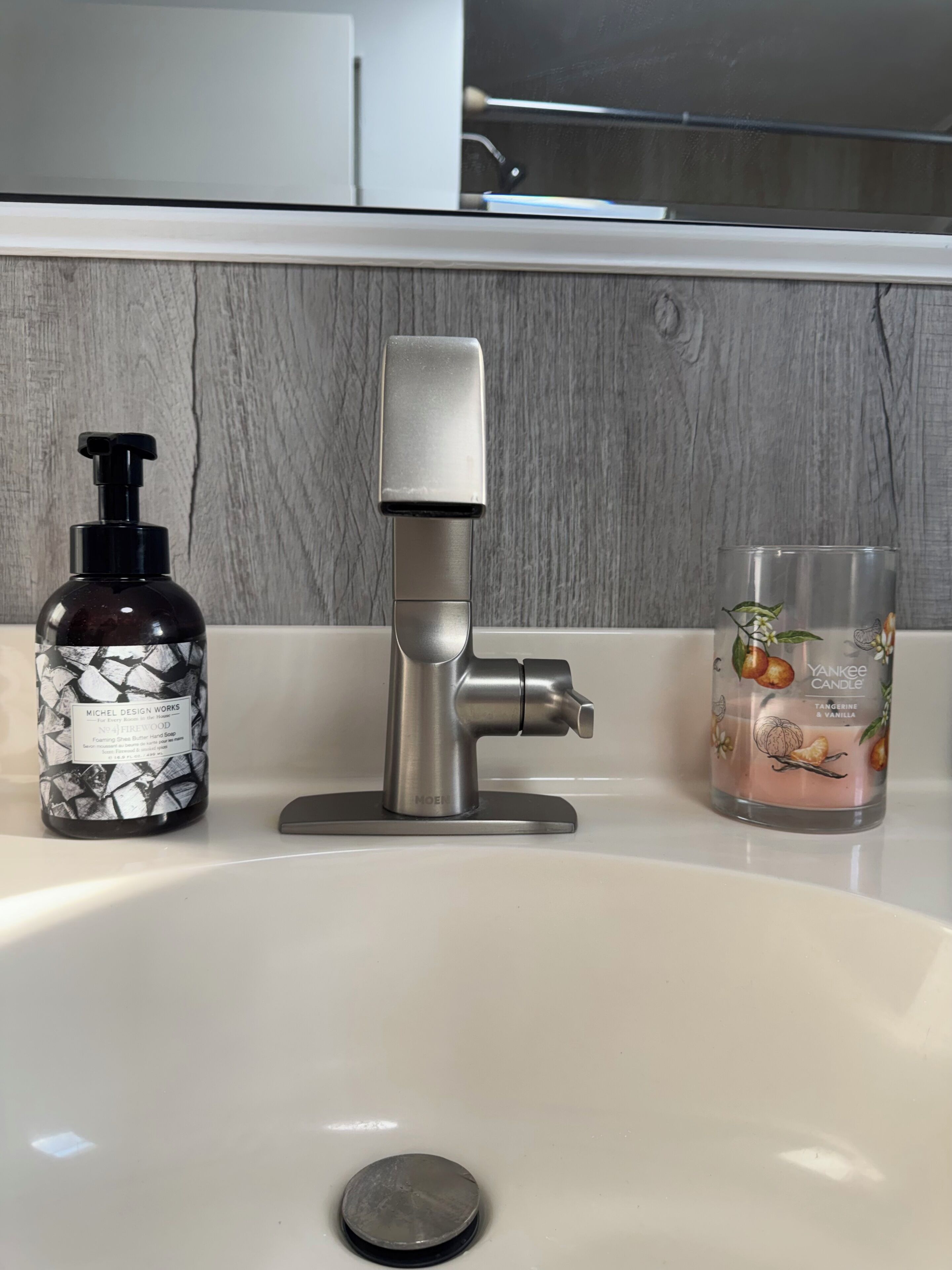A bathroom sink with a modern faucet, a soap dispenser, and a candle.