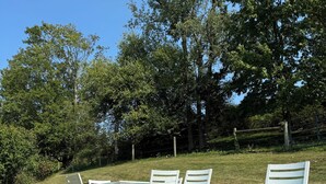 Un espacio al aire libre con asientos de césped, sillas de metal blanco y un carretón amarillo.