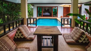 Ein Sitzbereich am Pool mit Tisch, gepolsterten Sofas und Blick auf ein Schlafzimmer mit Bett und Vorhängen.