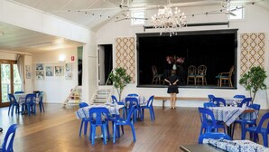 Um quarto com cadeiras e mesas azuis, um palco com cadeiras e um candelabro.