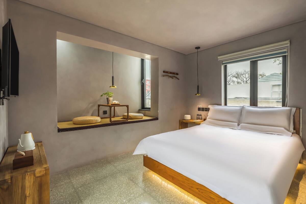 Une chambre moderne avec un grand lit, un banc intégré près de la fenêtre, une télévision et des lampes suspendues.