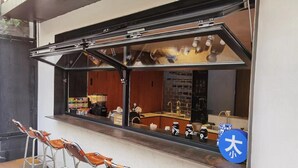 Ein Café mit großem Fenster, Metallstühlen und einem blauen Schild mit japanischen Schriftzeichen.