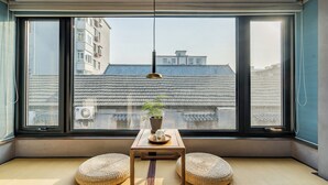 Ein Zimmer mit einem großen Fenster, einem kleinen Tisch mit einem Blumentopf und zwei runden Kissen.