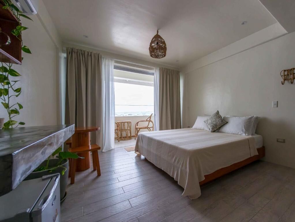 A bedroom with a bed, a desk, a chair, a window with curtains, and a hanging light fixture.