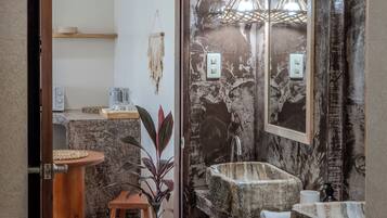 A bathroom with a rustic design, featuring a stone sink, a wooden stool, and a potted plant.