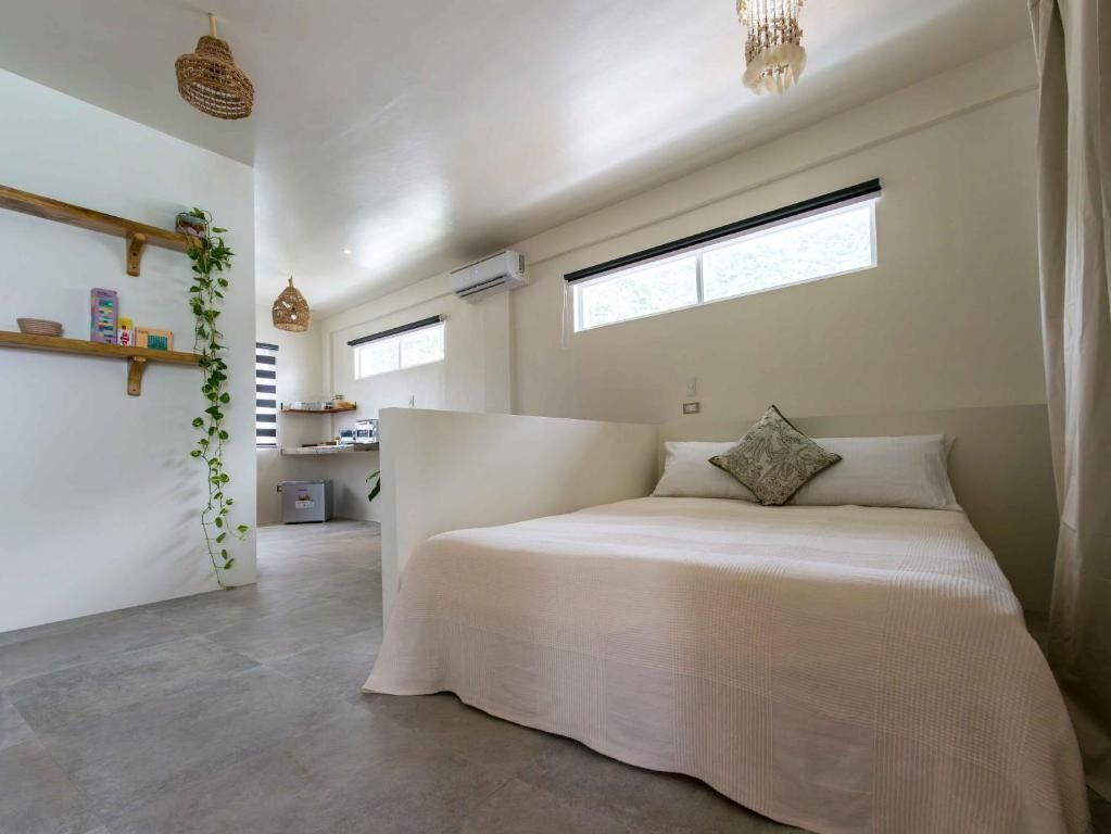 A bedroom with a large bed, a hanging light fixture, a window, and a plant.